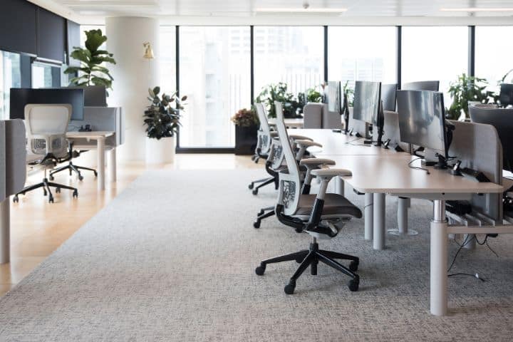 Ein gereinigtes Büro mit Schreibtischen und Stühlen vor großen Fenstern.