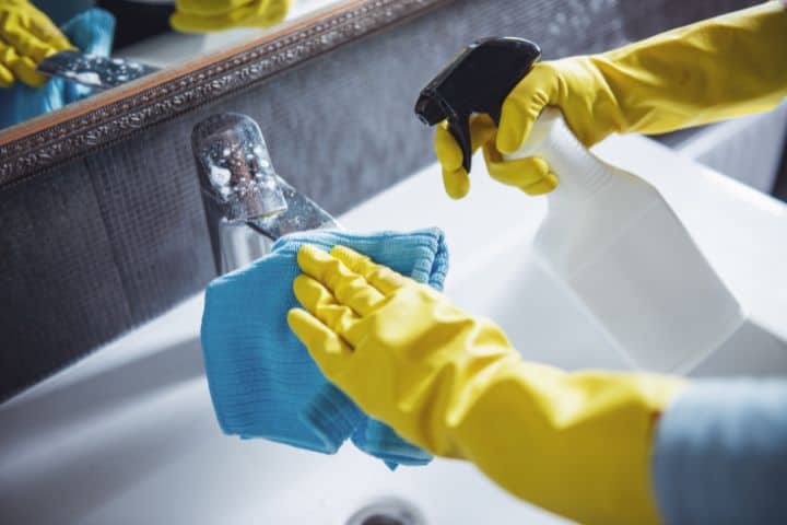 Eine Person mit gelben Handschuhen reinigt ein Waschbecken im Badezimmer.